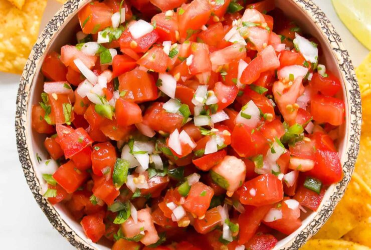 A rustic bowl of vibrant fresh pico de gallo with diced tomatoes, white onion, green jalapeño, and cilantro, shot overhead on a wooden board with tortilla chips alongside