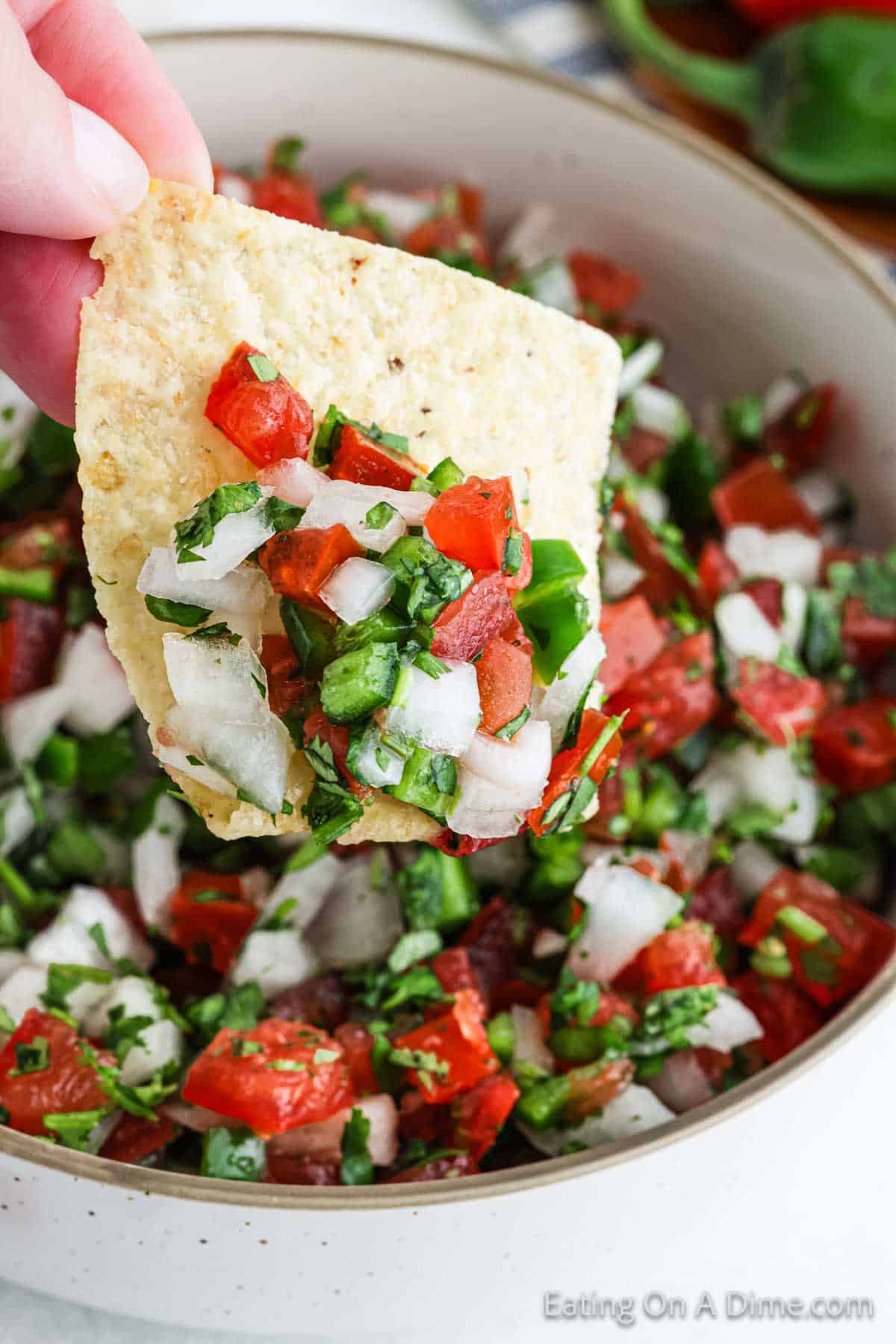 A close-up shot of fresh pico de gallo being scooped with a tortilla chip, showing the chunky texture of diced tomatoes, onion, and jalapeño glistening with lime juice