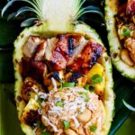 Huli Huli Chicken glazed with pineapple BBQ sauce plated on a wooden board with grilled pineapple slices and fresh herbs