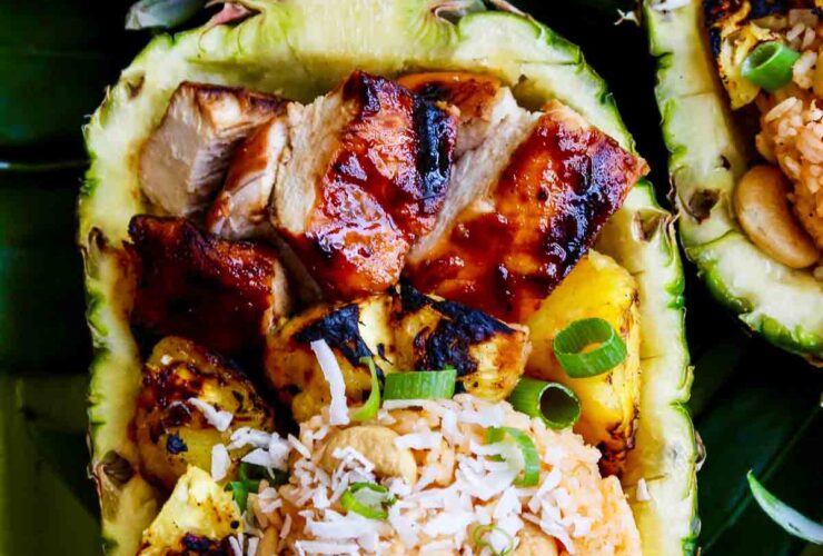 Huli Huli Chicken glazed with pineapple BBQ sauce plated on a wooden board with grilled pineapple slices and fresh herbs