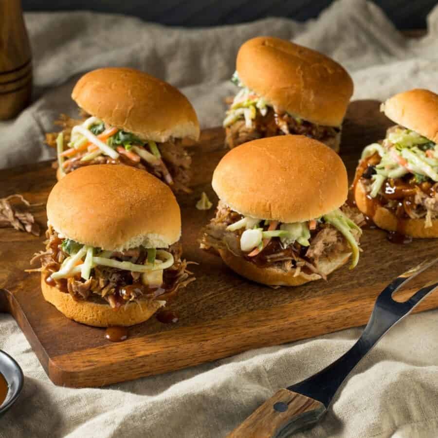 Instant Pot Pulled Pork for Camping — Make-Ahead Sliders from the Cooler 26 Instant pot pulled pork for camping served on slider buns with coleslaw on a wooden picnic table outdoors, golden hour light