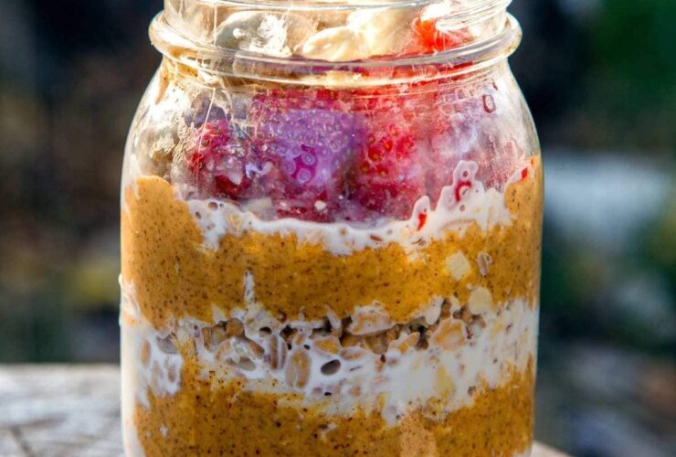 Overnight Camping Oatmeal — The Easy, Nourishing Breakfast You Prep Before You Even Leave Home 30 A rustic enamel camping mug filled with creamy overnight camping oatmeal topped with dried cranberries, chopped walnuts, and a drizzle of honey, set on a wooden picnic table with a campfire blurred in the background
