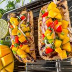 Peach mango salsa served in a rustic bowl garnished with fresh cilantro and lime wedges, with a grilled fish fillet topped with salsa on a white plate in the background