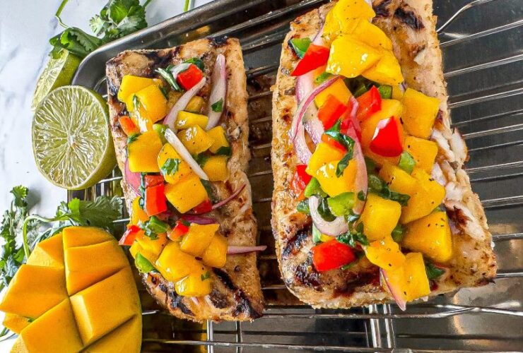Peach mango salsa served in a rustic bowl garnished with fresh cilantro and lime wedges, with a grilled fish fillet topped with salsa on a white plate in the background