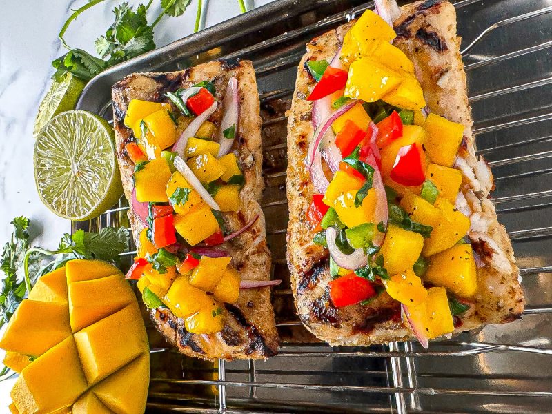 Peach mango salsa served in a rustic bowl garnished with fresh cilantro and lime wedges, with a grilled fish fillet topped with salsa on a white plate in the background