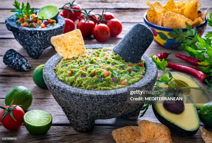 restaurant style guacamole served in a stone molcajete bowl with tortilla chips, fresh lime wedges, and cilantro garnish on a rustic wooden board