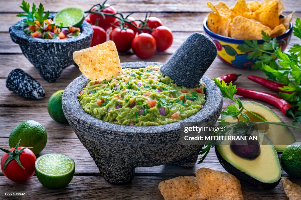 restaurant style guacamole served in a stone molcajete bowl with tortilla chips, fresh lime wedges, and cilantro garnish on a rustic wooden board