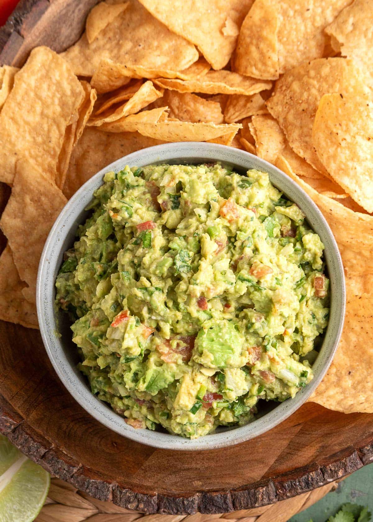 close-up of restaurant style guacamole in a rustic bowl with a tortilla chip being dipped in, showing chunky texture and bright green color with visible lime zest and cilantro