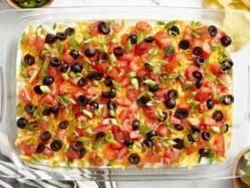 Seven Layer Dip — The Ultimate Party Platter Classic with Chips 36 Seven Layer Dip beautifully plated in a wide glass dish with colorful layers of beans, sour cream, guacamole, cheese, tomatoes, olives, and green onions served with tortilla chips