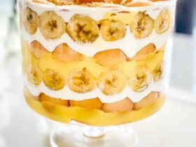 Classic banana pudding served in a wide glass trifle bowl, showing beautiful layers of vanilla wafers, fresh banana slices, and creamy custard topped with billowy whipped cream and wafer crumbles