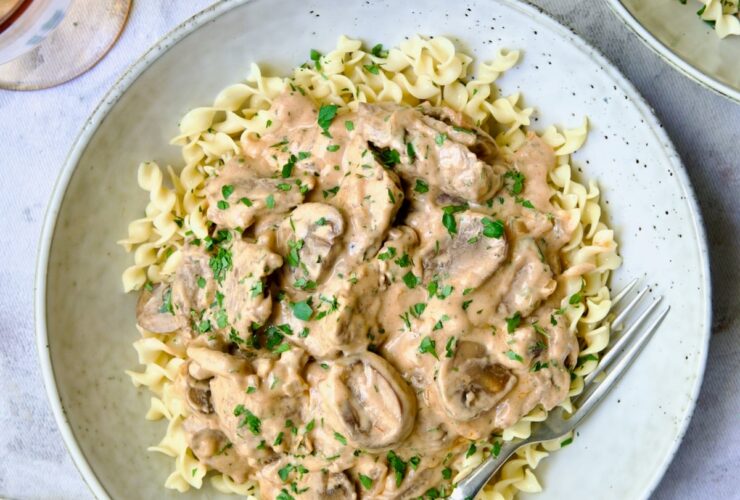 Beef Stroganoff served in a wide bowl over egg noodles, garnished with fresh parsley, rich creamy mushroom sauce visible