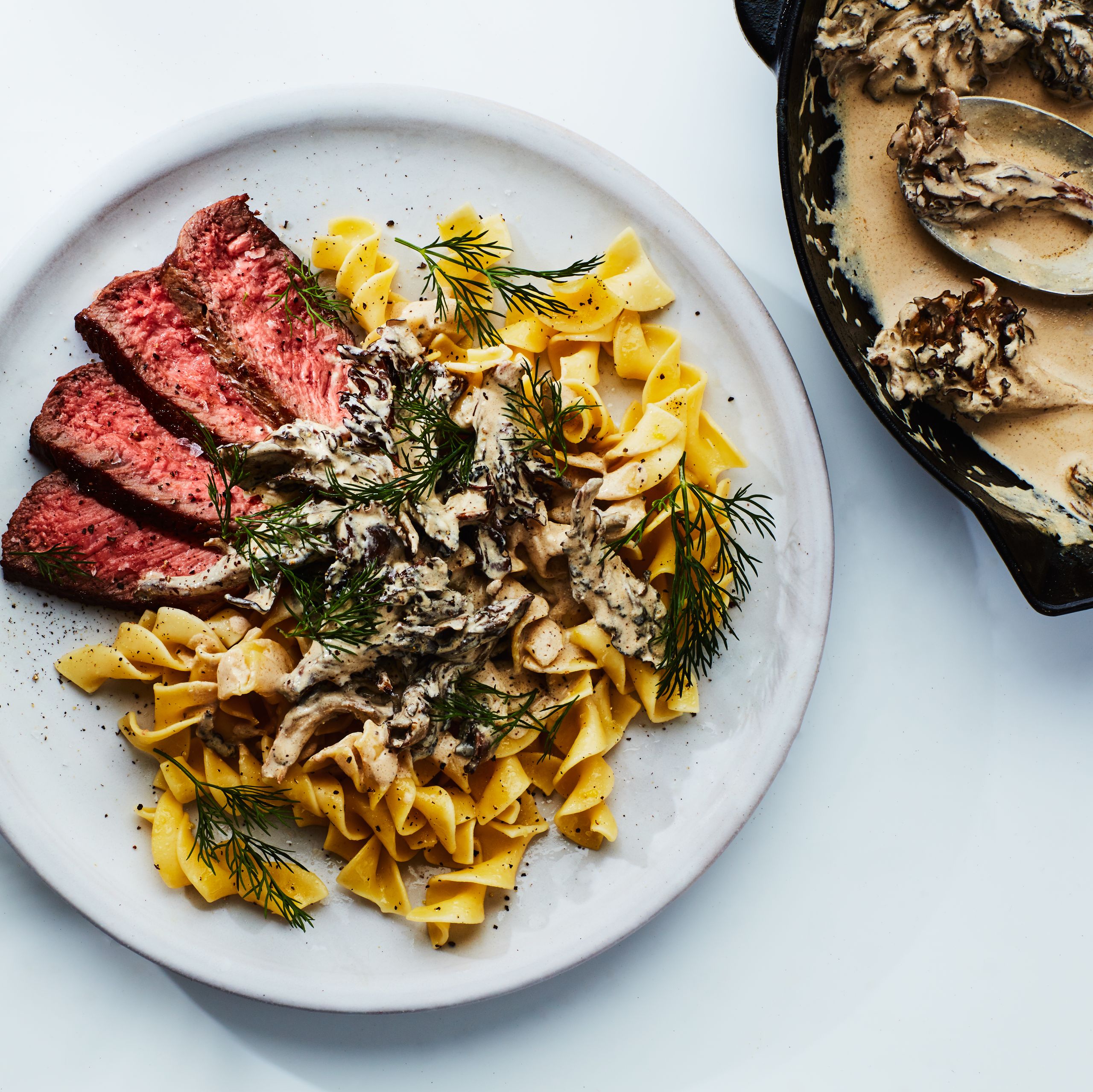 Ingredients for Beef Stroganoff laid out flat — sliced sirloin, cremini mushrooms, sour cream, beef broth, onion, garlic, Dijon mustard, and egg noodles