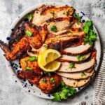 Beer Can Chicken with golden crispy skin resting on a cutting board surrounded by fresh herbs and lemon halves