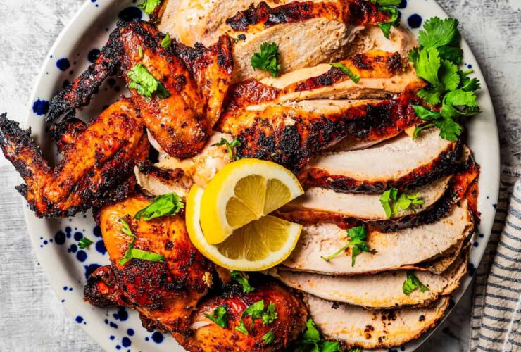 Beer Can Chicken with golden crispy skin resting on a cutting board surrounded by fresh herbs and lemon halves