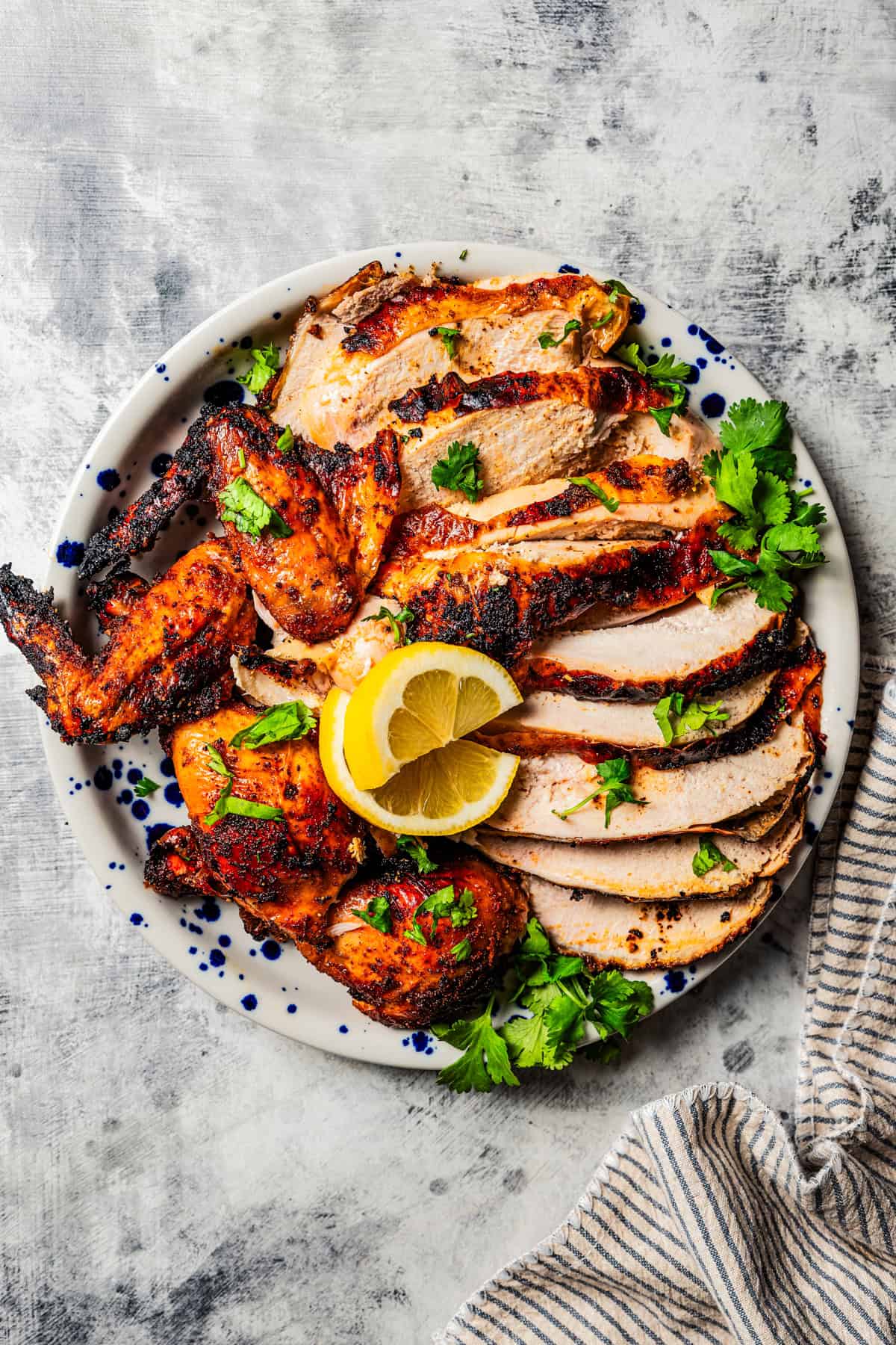 Beer Can Chicken with golden crispy skin resting on a cutting board surrounded by fresh herbs and lemon halves