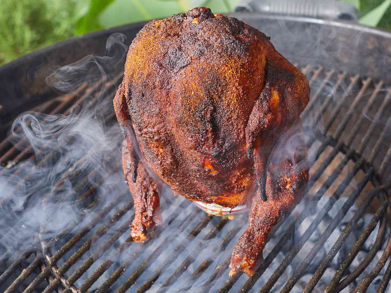 Beer Can Chicken prep shot showing whole chicken being rubbed with spices next to a can of beer, olive oil, and bowls of dry rub spices on a wooden surface