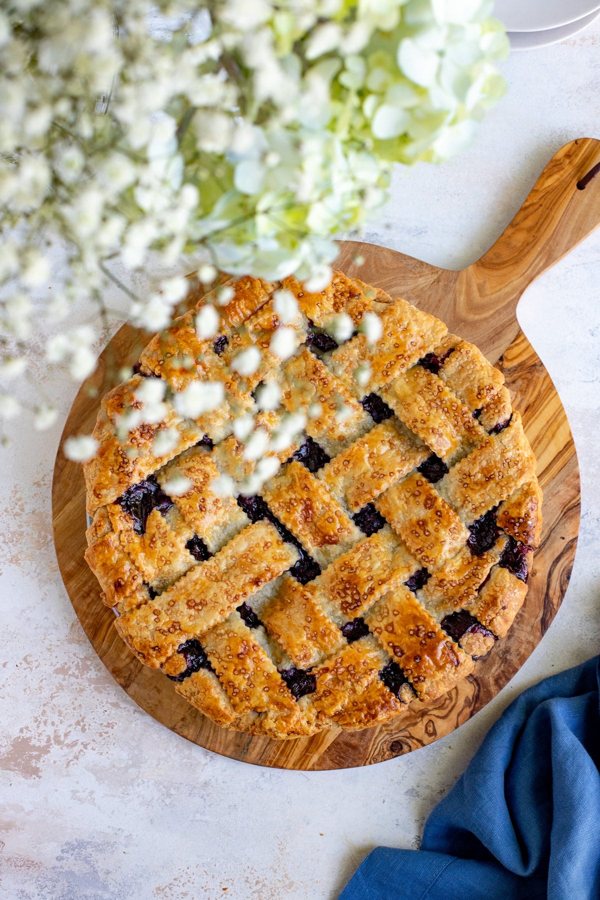 golden lattice top blueberry pie cooling on a wooden table surrounded by fresh blueberries and a vintage pie server