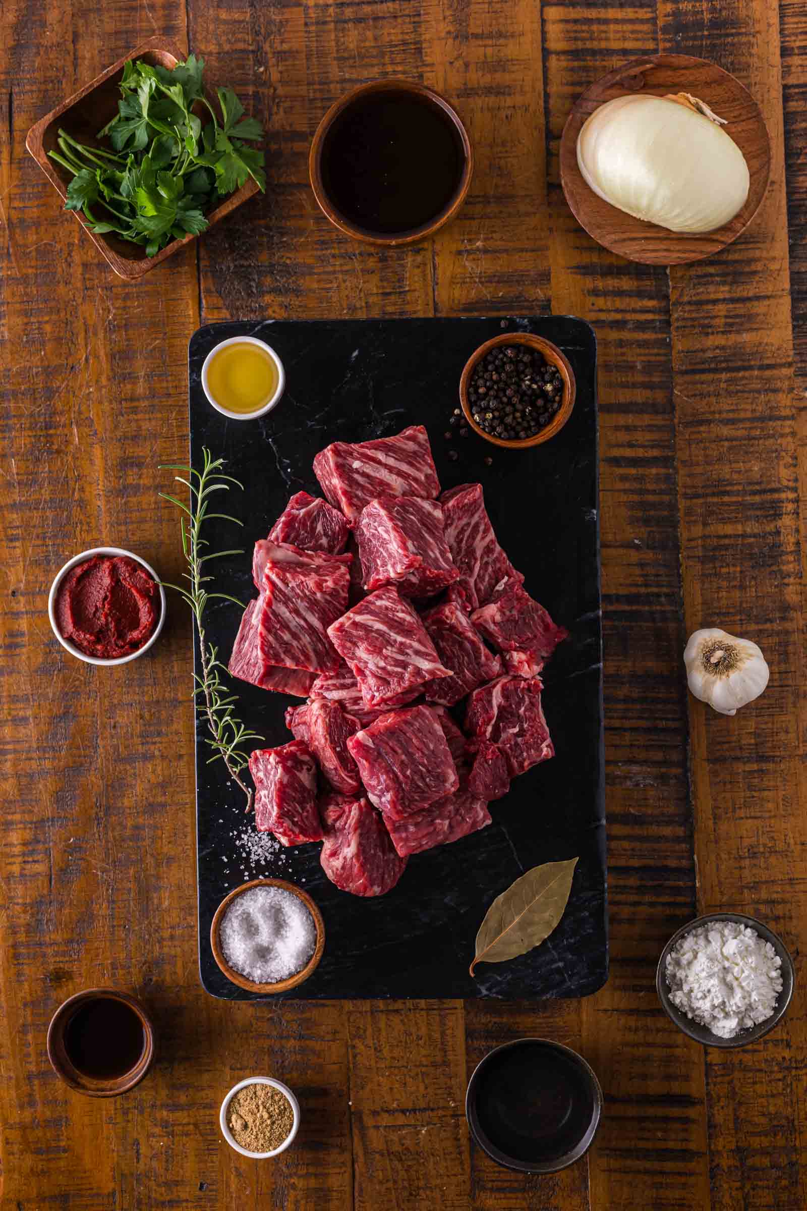 Ingredients for Crockpot Beef and Noodles laid out on a wooden board including chuck roast, egg noodles, beef broth, garlic, onion, and seasonings