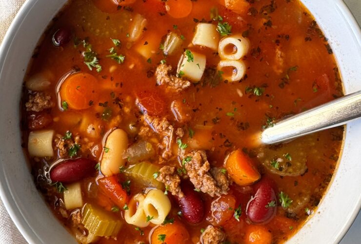 A steaming bowl of Crockpot Pasta e Fagioli with ground beef, cannellini beans, and ditalini pasta in a rich tomato broth, garnished with fresh parsley and Parmesan, photographed on a rustic wooden table