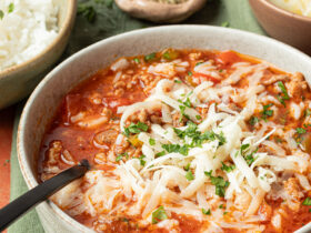 Crockpot Stuffed Pepper Soup — All the Comfort of Stuffed Peppers in One Easy Bowl 40 A rustic white bowl filled with Crockpot Stuffed Pepper Soup topped with shredded cheese and fresh parsley, set on a wooden table with a slow cooker in the background