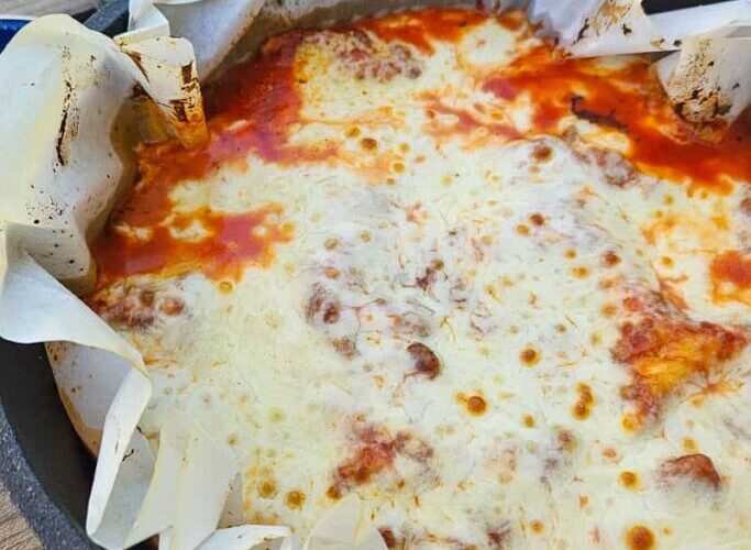 Dutch Oven Lasagna served from a cast iron Dutch oven at a campsite, bubbling with melted cheese and rich tomato sauce, golden and rustic