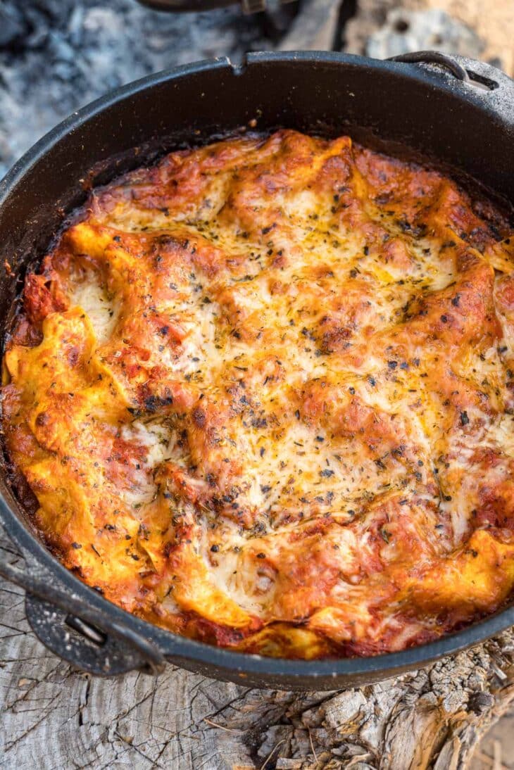 Close-up of a scoop of Dutch Oven Lasagna being lifted from the cast iron pot showing distinct layers of pasta, sausage, ricotta, and melted mozzarella cheese