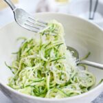 Garlic Parmesan Zoodles served in a wide white bowl, topped with freshly grated Parmesan and chopped parsley, with a fork twirling the zucchini noodles, soft natural light, food photography