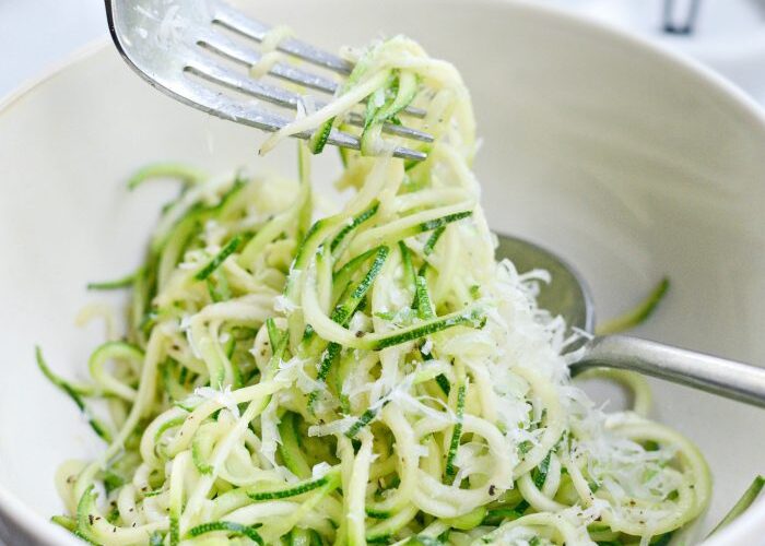 Garlic Parmesan Zoodles served in a wide white bowl, topped with freshly grated Parmesan and chopped parsley, with a fork twirling the zucchini noodles, soft natural light, food photography