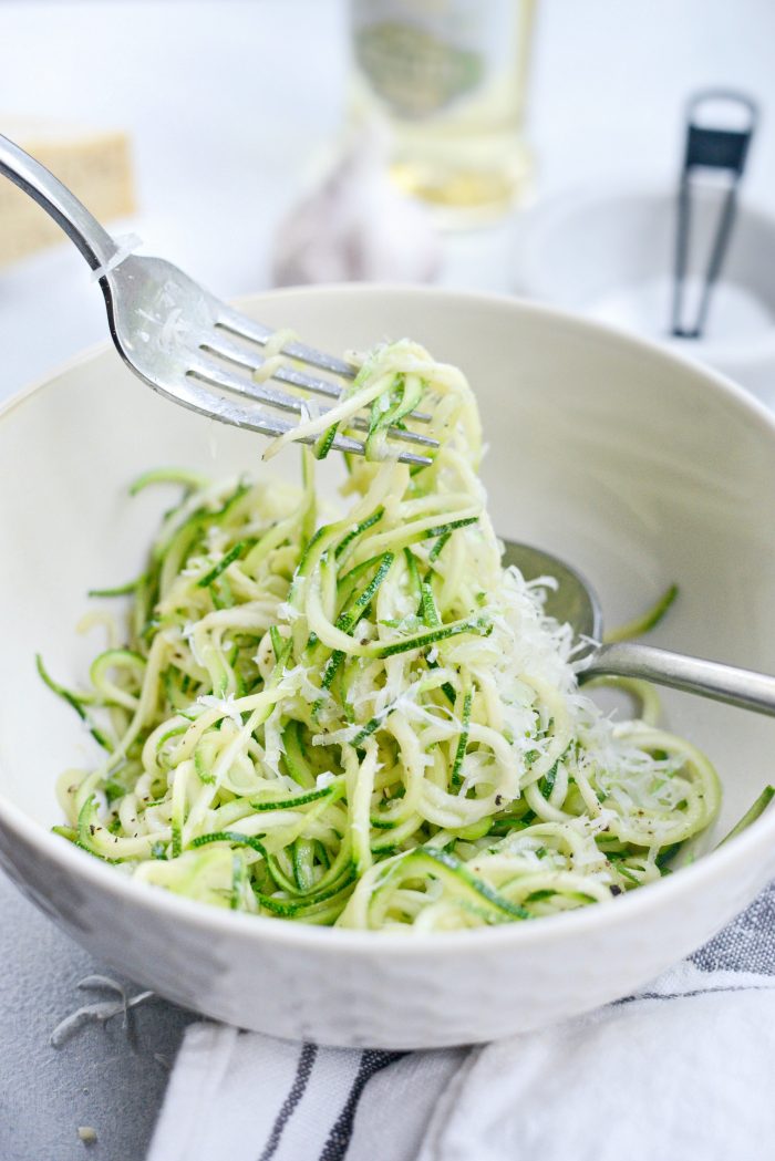 Garlic Parmesan Zoodles served in a wide white bowl, topped with freshly grated Parmesan and chopped parsley, with a fork twirling the zucchini noodles, soft natural light, food photography