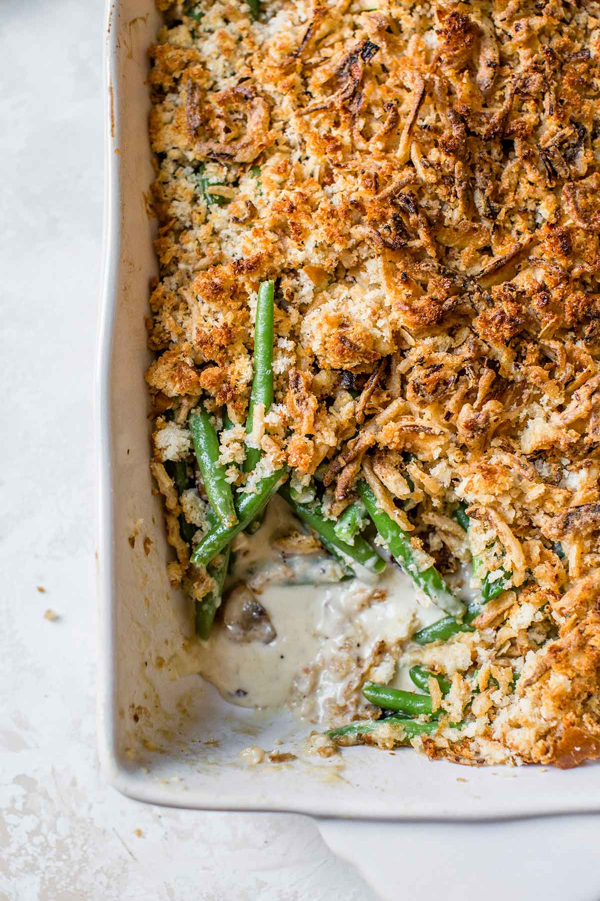 Green Bean Casserole — The Classic Comfort Dish Made Cleaner & Better 26 A beautifully plated green bean casserole in a white ceramic baking dish, topped with golden crispy fried onions, set on a rustic wooden table with autumn leaves in the background