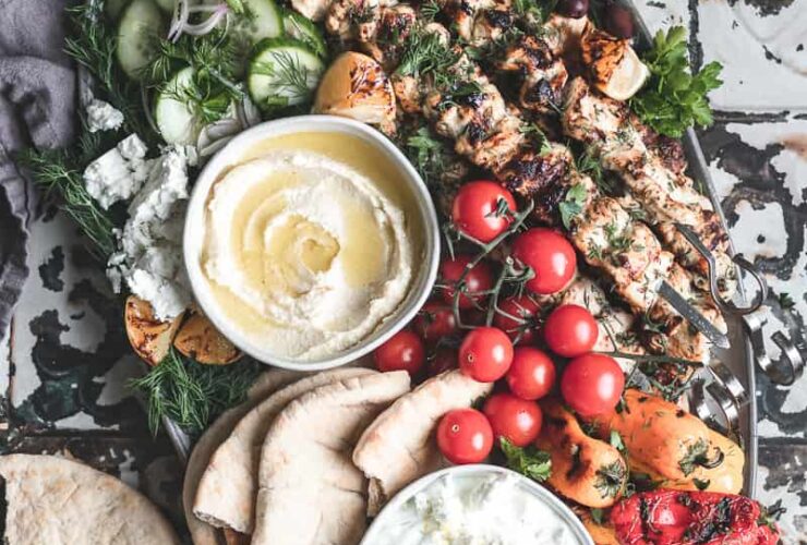 Grilled chicken skewers with tzatziki served on a wooden platter with pita, lemon wedges, and fresh herbs at a campsite