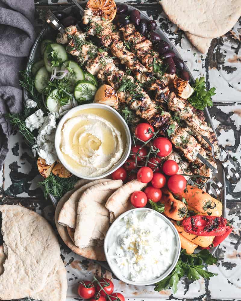 Grilled Chicken Skewers with Tzatziki — Greek-Inspired Camp Grill Recipe 26 Grilled chicken skewers with tzatziki served on a wooden platter with pita, lemon wedges, and fresh herbs at a campsite