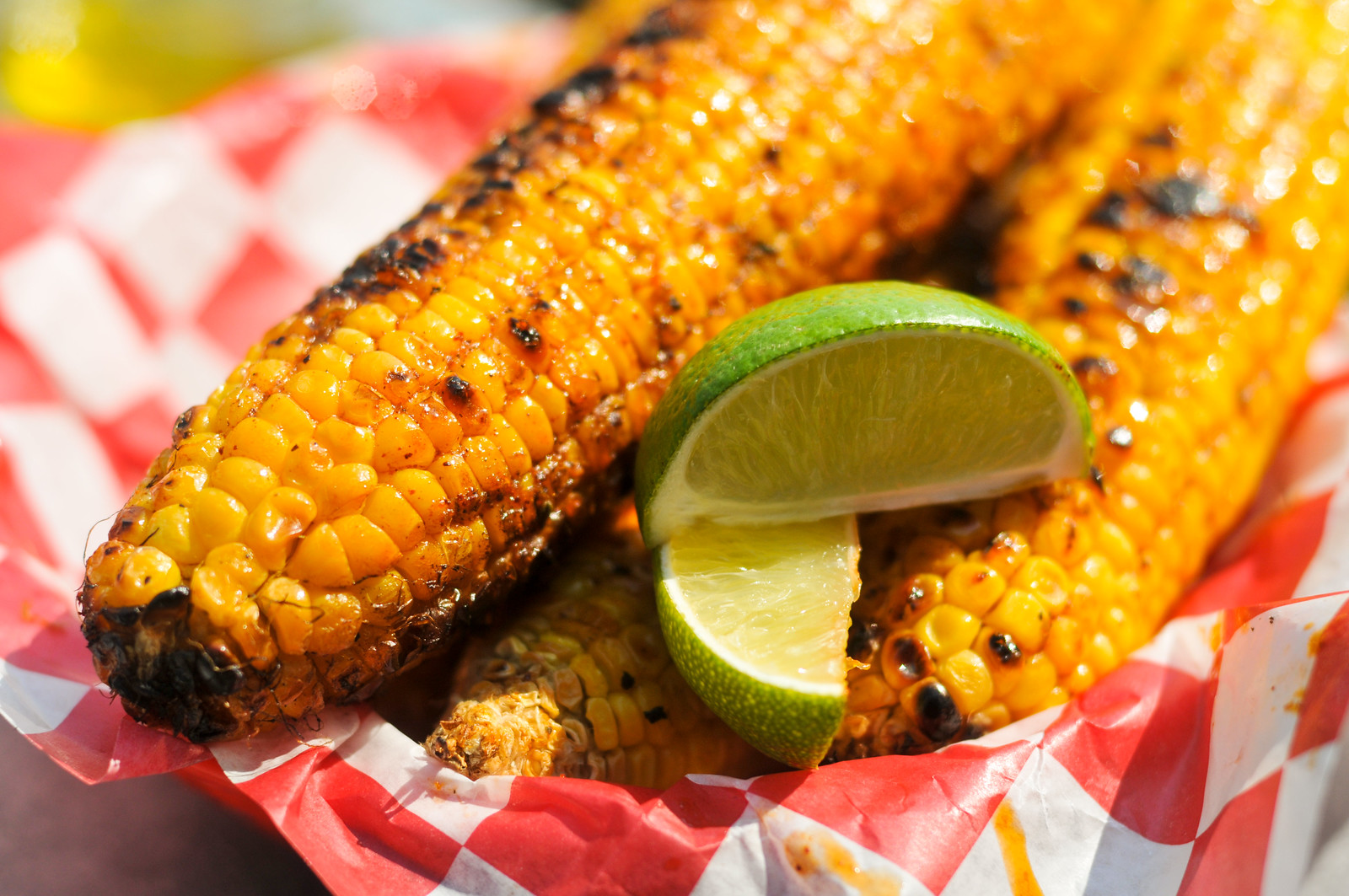 Fresh ears of corn, compound herb butter, grated Parmesan, chili powder, lime wedges, and smoked paprika arranged as flat lay ingredients on a marble surface