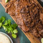 Grilled flank steak sliced thin and arranged on a wooden board surrounded by warm corn tortillas, fresh lime wedges, diced white onion, cilantro, and sliced avocado, shot on a rustic table with warm natural light