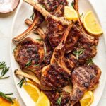 beautifully plated grilled lamb chops with rosemary garlic herb crust on a wooden board with lemon wedges and fresh herbs