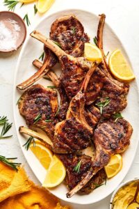beautifully plated grilled lamb chops with rosemary garlic herb crust on a wooden board with lemon wedges and fresh herbs