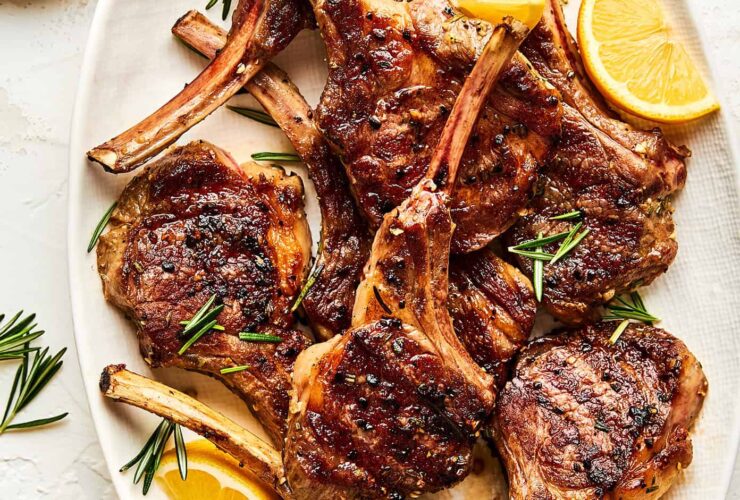beautifully plated grilled lamb chops with rosemary garlic herb crust on a wooden board with lemon wedges and fresh herbs