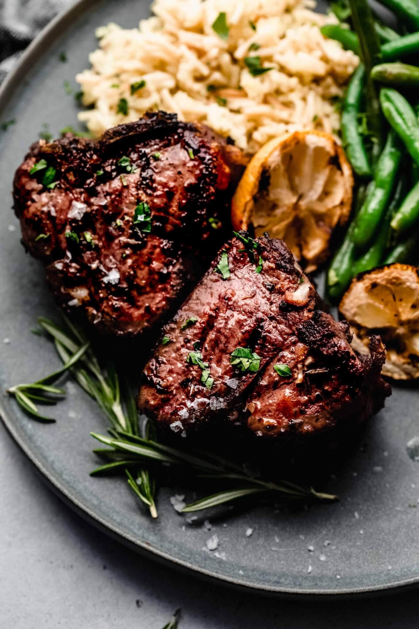grilled lamb chops marinade ingredients flatlay with rosemary, garlic, lemon, olive oil, and Dijon mustard on a marble surface