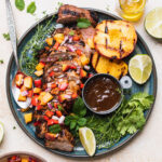 Beautifully plated grilled pork tenderloin sliced on a wooden cutting board with fresh herb garnish, charred grill marks visible, served alongside roasted vegetables