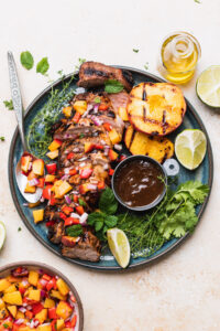 Beautifully plated grilled pork tenderloin sliced on a wooden cutting board with fresh herb garnish, charred grill marks visible, served alongside roasted vegetables