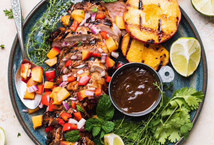Beautifully plated grilled pork tenderloin sliced on a wooden cutting board with fresh herb garnish, charred grill marks visible, served alongside roasted vegetables