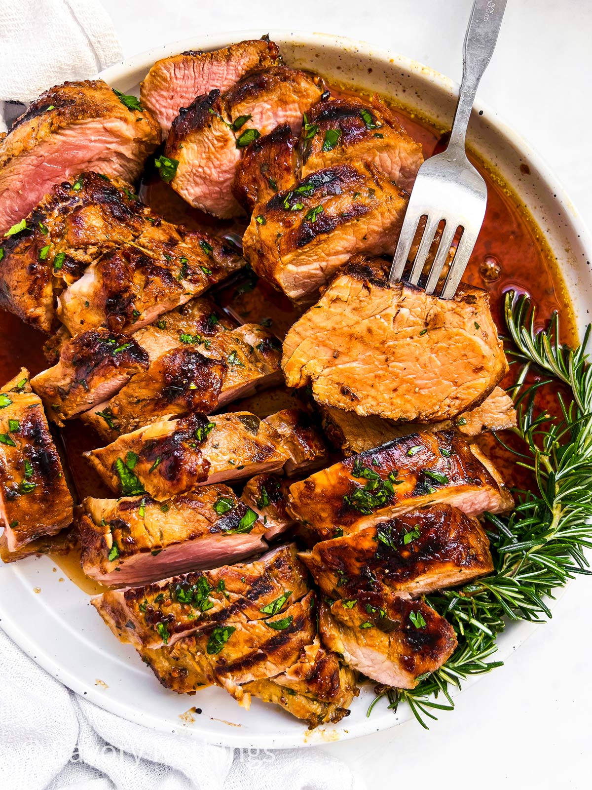 Overhead flat lay of grilled pork tenderloin marinade ingredients — olive oil, garlic, Dijon mustard, fresh rosemary, thyme, honey, smoked paprika arranged on a marble surface
