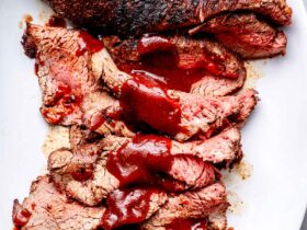 Perfectly grilled tri-tip steak sliced on a wooden cutting board with a smoky crust, pink interior, and fresh herbs scattered around