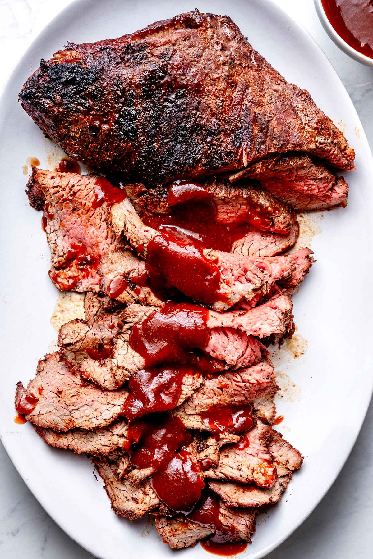 Perfectly grilled tri-tip steak sliced on a wooden cutting board with a smoky crust, pink interior, and fresh herbs scattered around