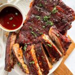 Fall-off-the-bone Instant Pot ribs glazed with BBQ sauce, sliced and plated on a wooden board with fresh herbs and a side of coleslaw
