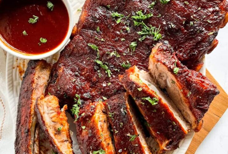 Fall-off-the-bone Instant Pot ribs glazed with BBQ sauce, sliced and plated on a wooden board with fresh herbs and a side of coleslaw