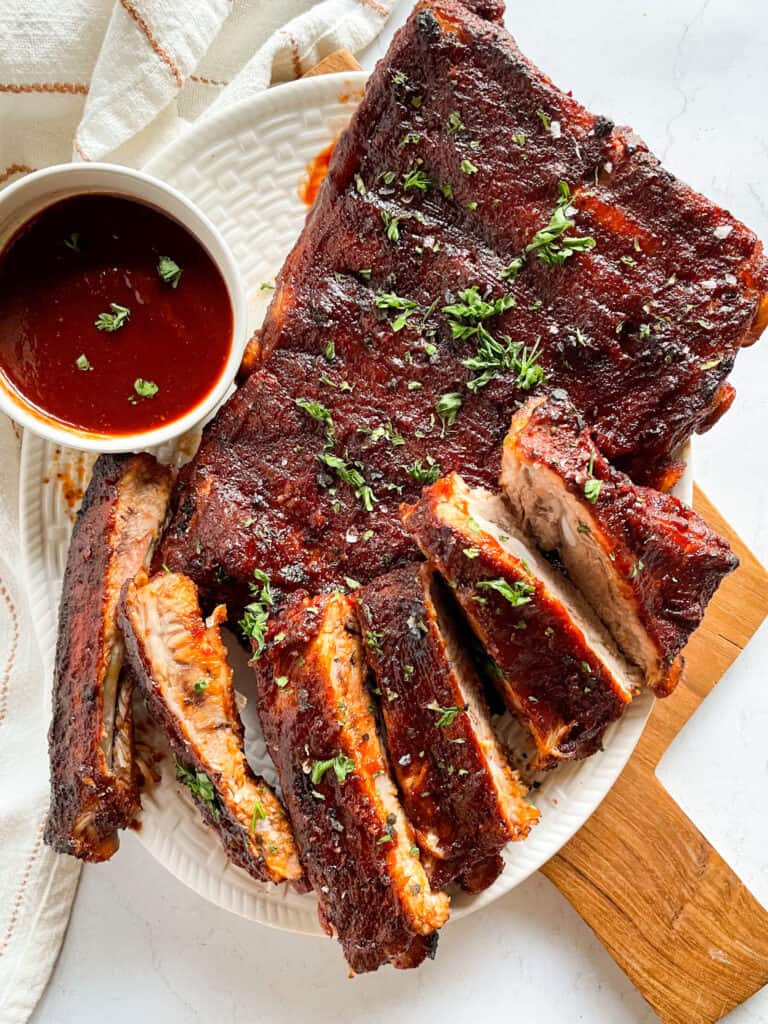 Instant Pot Ribs — Fall-Off-The-Bone Tender in Under an Hour 26 Fall-off-the-bone Instant Pot ribs glazed with BBQ sauce, sliced and plated on a wooden board with fresh herbs and a side of coleslaw