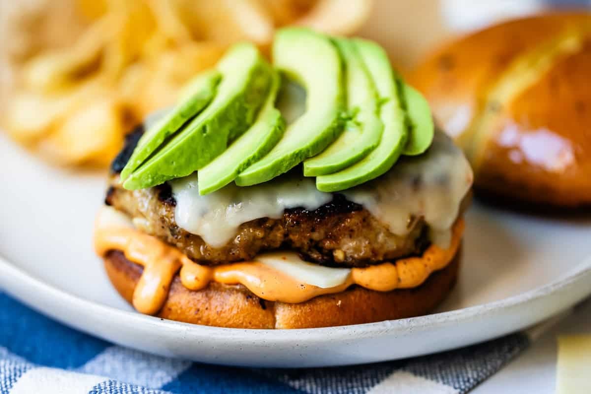 Close-up of a sliced juicy turkey burger showing the interior texture, topped with melted cheddar, avocado slices, and fresh arugula on a toasted whole wheat bun