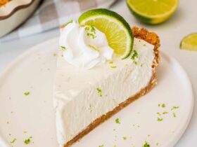 Classic Key Lime Pie with golden graham cracker crust, creamy pale yellow filling, and swirled whipped cream topping on a white plate with fresh lime slices