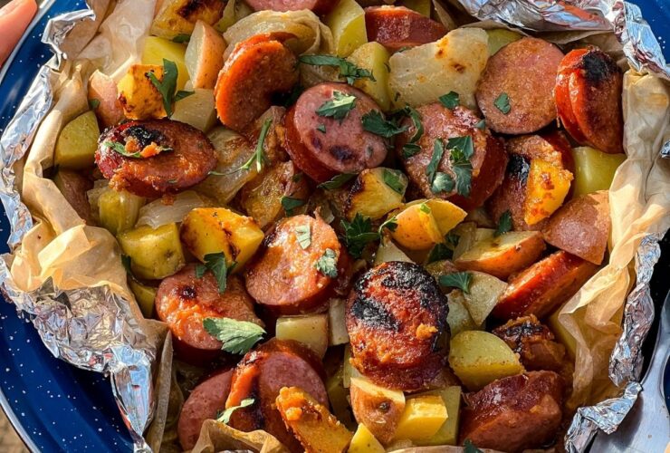 Kielbasa and potato foil packets opened on a plate showing golden sausage slices and tender potatoes with a glossy mustard glaze, garnished with fresh parsley